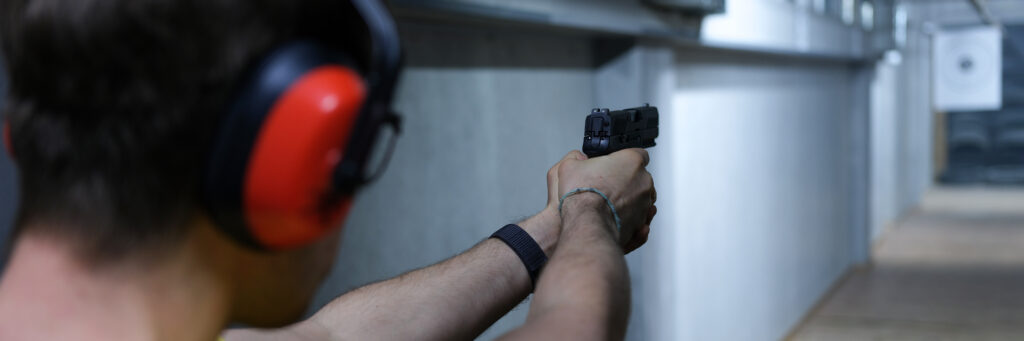 Male target shooter in headphones aiming pistol at target in shooting range